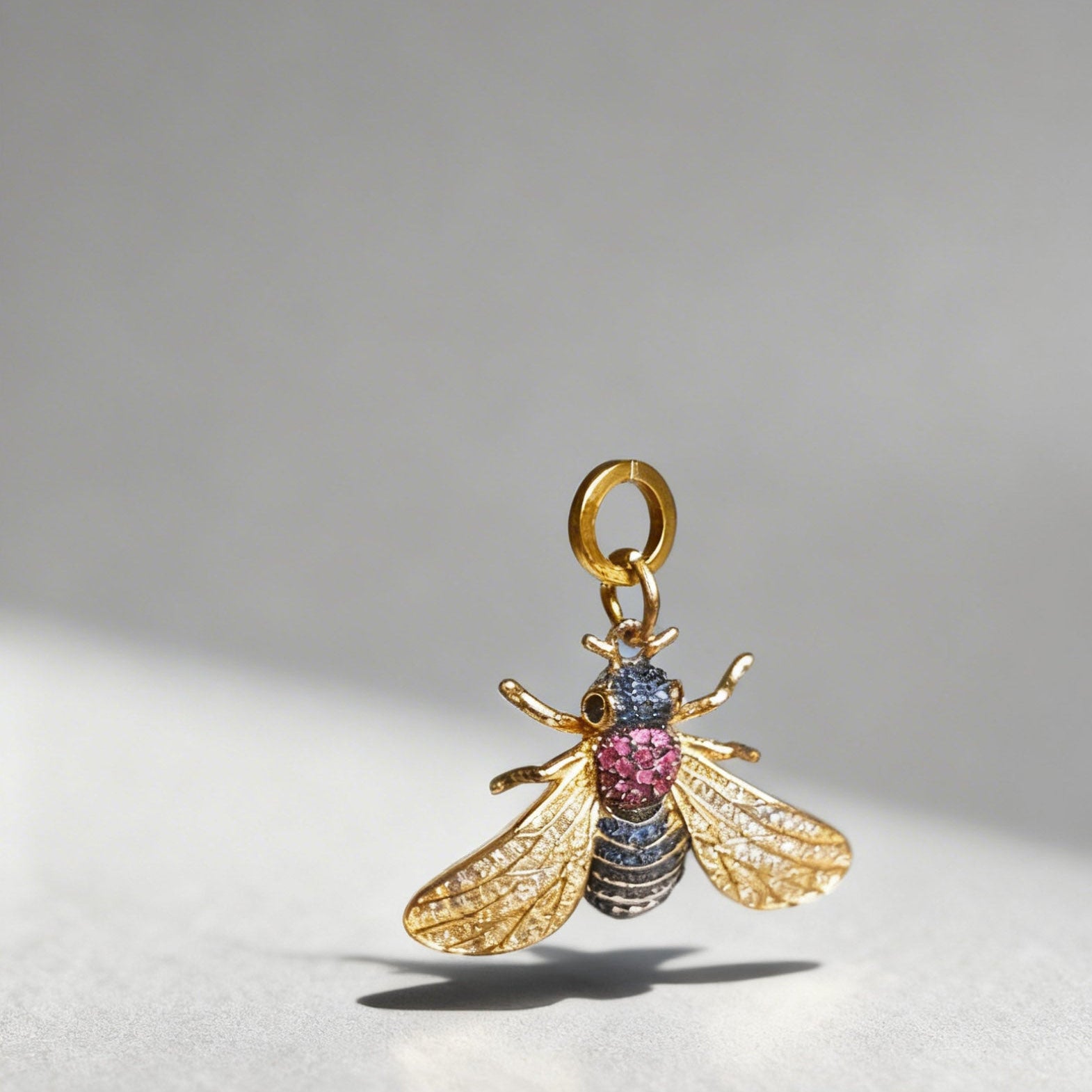 Gold bee-shaped pendant with gemstones on a gray background